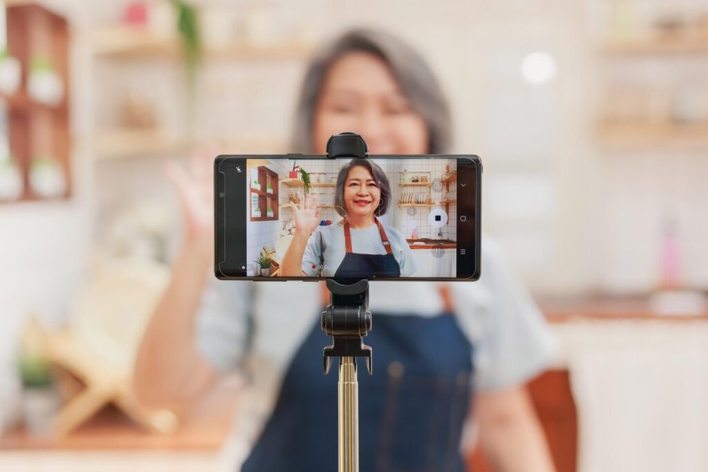 A woman with a phone mounted in front of her, waving to the camera. Only the phone is in focus.